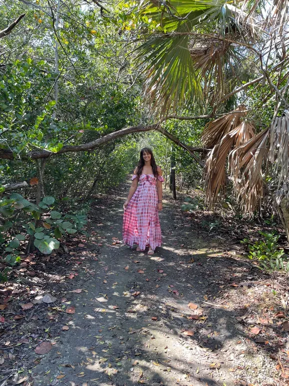 Jen standing on a sunlit nature trail beneath green trees